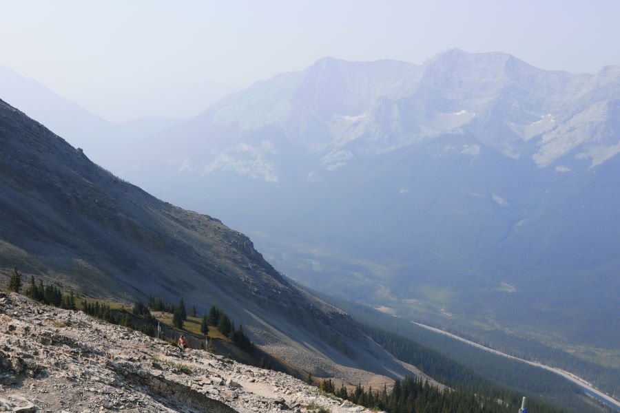 person hiking in front of hazy mountains on the final stretch of the saddle of Ha Ling Peak trail, ascending towards the summit
