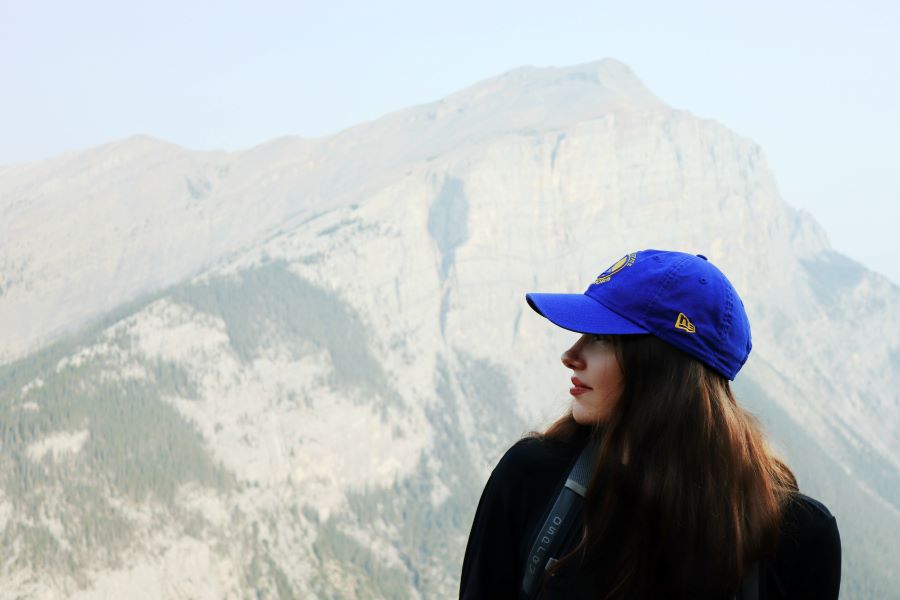 person in a blue cap standing for a profile portrait photograph in front of a hazy afternoon Mount Rundle along the ascent of Ha Ling Peak trail